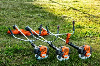 Three grass trimmers placed on a lawn, ready for use.