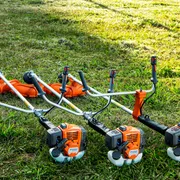 Three grass trimmers placed on a lawn, ready for use.