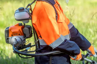 A person operating a brush cutter in a grassy area.