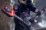 Uma pessoa a utilizar um aparador a bateria da Husqvarna num ambiente exterior.