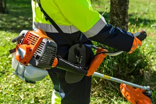 A person using a grass trimmer in a garden setting.