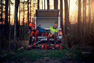 Två arbetare som förbereder Husqvarna-produkter från ett fordon i en skogsmiljö.