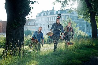 Three workers walking through a grassy area carrying string trimmers.