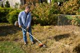 A person using a string trimmer to cut grass along a fence in a garden.