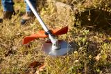 A person using a grass trimmer to clear overgrown grass and weeds in a garden.