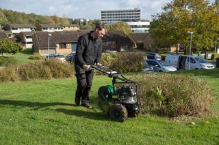 A person using a lawn aerator on a grassy slope in a residential area.