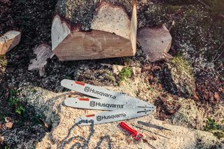 Two Husqvarna chainsaw bars and a wrench on a tree stump in a forest setting.