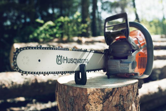 A Husqvarna chainsaw resting on a tree stump in a forest setting.