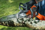Close-up of a person cutting a tree branch with a Husqvarna chainsaw, wood chips flying.