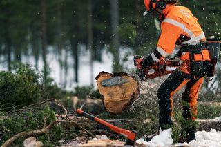 En person som använder en motorsåg för att såga en stock i en snöig skogsmiljö.