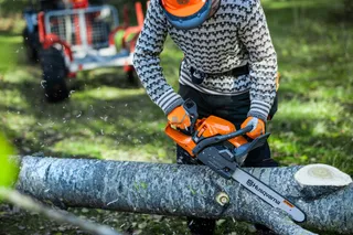 En person som använder en motorsåg från Husqvarna för att såga ett nedfallet träd i en skogsmiljö.