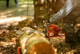 A person using a chainsaw to cut a log in a forest setting.