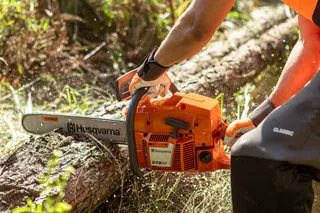 A person using a chainsaw to cut a log outdoors.