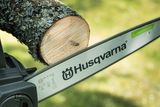 Close-up of a Husqvarna chainsaw bar cutting through a tree branch outdoors.