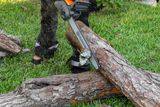 A person using a Husqvarna chainsaw to cut a fallen tree log on grass.
