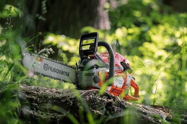 A Husqvarna chainsaw resting on a fallen tree trunk in a forest setting.