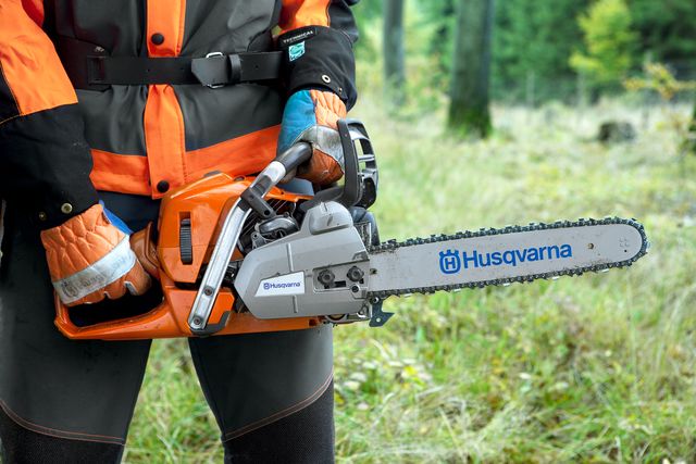 Una persona sosteniendo una motosierra Husqvarna en un bosque.