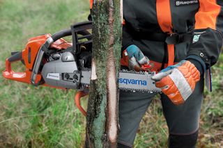 A person using a Husqvarna chainsaw to cut a tree trunk outdoors.