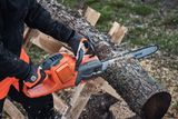 Oseba, ki uporablja verižno žago Husqvarna za žaganje drevesnega hloda na prostem.