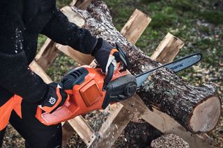 En person som bruker en motorsag til å kappe en stokk utendørs.