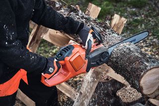 A person using a chainsaw to cut a log outdoors.
