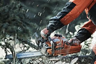Людина використовує ланцюгову пилку Husqvarna для зрізання гілки дерева на відкритому повітрі.