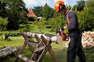 En person som bruker en motorsag til å kappe en stokk på en sagbukk i en hagesetting.