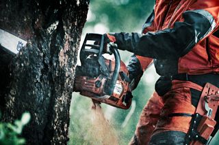 A person using a chainsaw to cut a tree trunk outdoors.