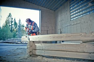 A person using a chainsaw to cut wooden logs in a workshop setting.