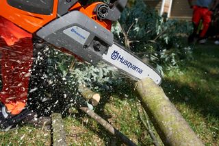 Ланцюгова пилка Husqvarna розпилює гілку дерева, і в неї відлітає тріска.