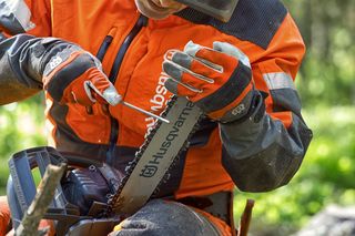 A person sharpening a Husqvarna chainsaw blade in a forest setting.