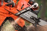 A person using a Husqvarna chainsaw to cut through a log, with wood chips flying.