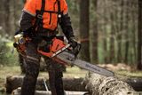 A person using a Husqvarna chainsaw to cut logs in a forest setting.