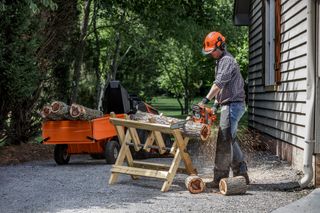 A person using a chainsaw to cut logs on a sawhorse, with a log splitter in the background.