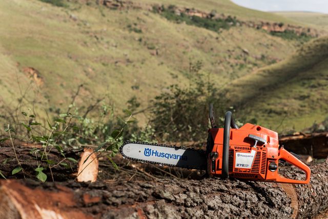 A Husqvarna chainsaw resting on a cut tree log in a hilly landscape.