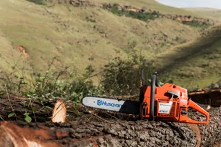 A Husqvarna chainsaw resting on a cut tree log in a hilly landscape.