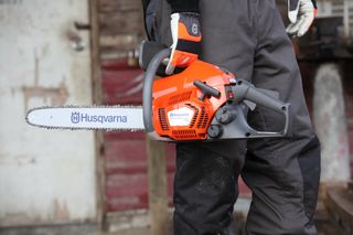 En person som holder en motorsag fra Husqvarna som viser frem produktet fra siden.