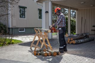 Osoba używająca piły łańcuchowej do cięcia kłód na koniu piły na podjeździe mieszkalnym.