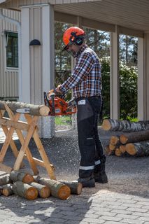 A person using a chainsaw to cut logs on a sawhorse in a residential driveway.