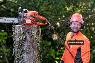 Une personne en tenue de travail assise sur une souche d’arbre avec une tronçonneuse Husqvarna.