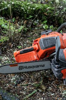 Two Husqvarna chainsaws resting on a forest floor, surrounded by wood chips and foliage.