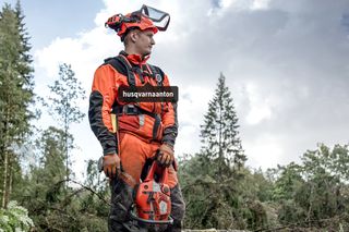 Une personne debout sur une souche d’arbre dans une forêt, tenant une tronçonneuse Husqvarna.