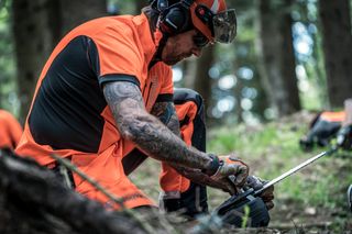 森の中でチェーンソーを調整する作業用具を着た人。