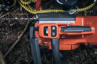 Close-up of a chainsaw handle and control buttons on a forest floor.