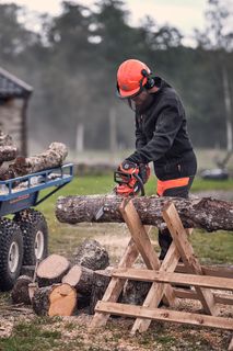 使用链锯在带拖车的全地形车旁边的锯木上切割原木的人。