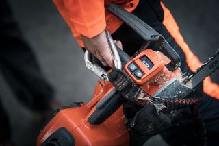 Person holding a chainsaw, focusing on the control panel and safety features.