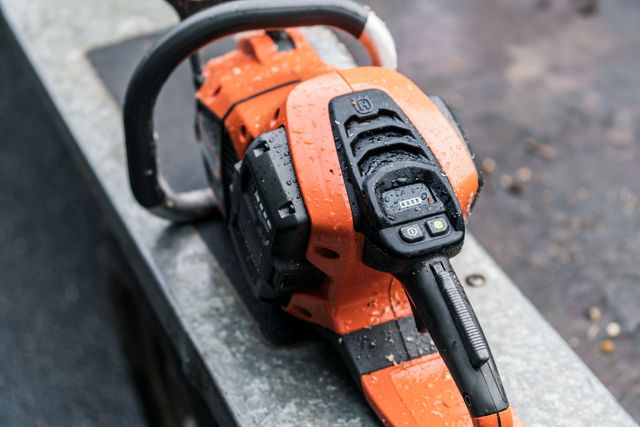 Közeli kép egy fémfelületen nyugvó Husqvarna láncfűrészről, amely bemutatja a kezelőpaneljét.