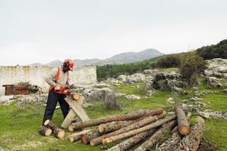 A person using a chainsaw to cut logs in a rural outdoor setting.