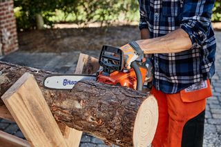 A person using a Husqvarna chainsaw to cut a tree log outdoors.