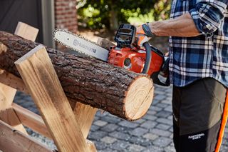 A person using a Husqvarna chainsaw to cut a log on a wooden stand.